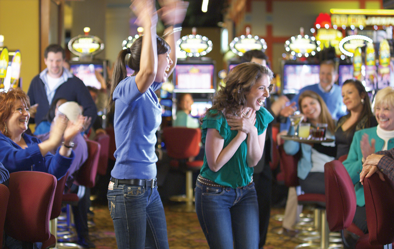 Two women standing up and cheering in front of slot machines