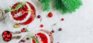 Red cocktails garnished with cranberries, rosemary and coconut.